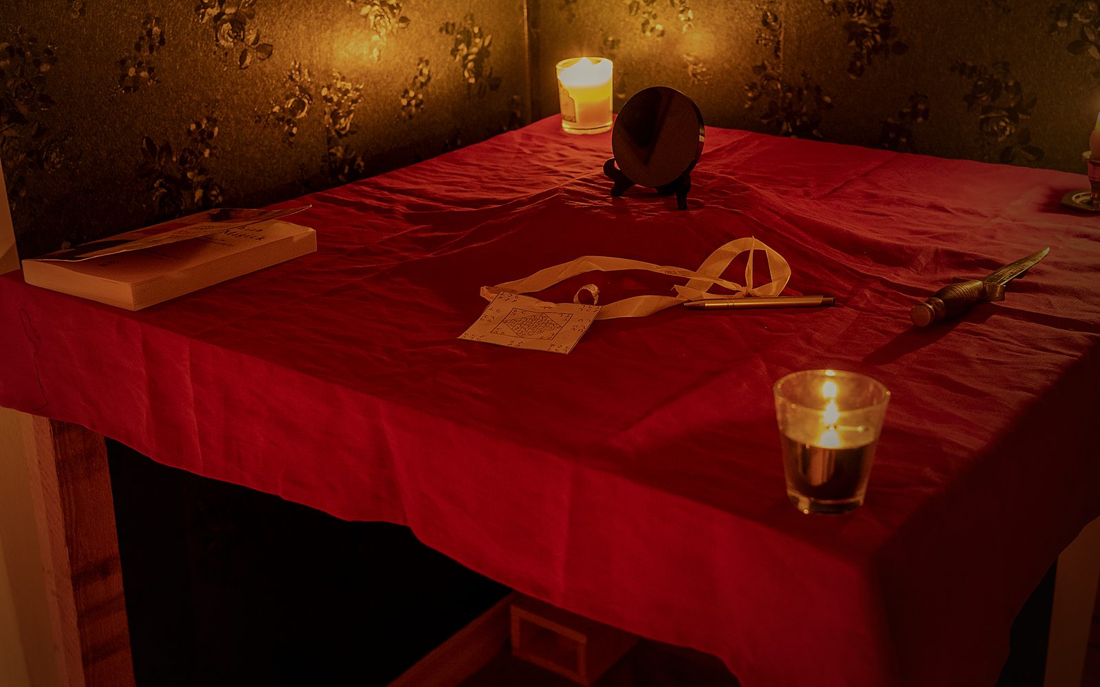 The Holy Table dressed for a working, lit only by hand-poured candles: the scrying mirror, the seal and the ceremonial blade in place